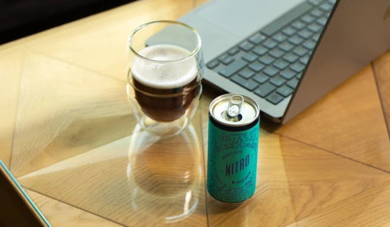 Why you should buy nitro cold brew coffee for your business 6 A cold brew coffee can next to a laptop and a glass with cold brew coffee.