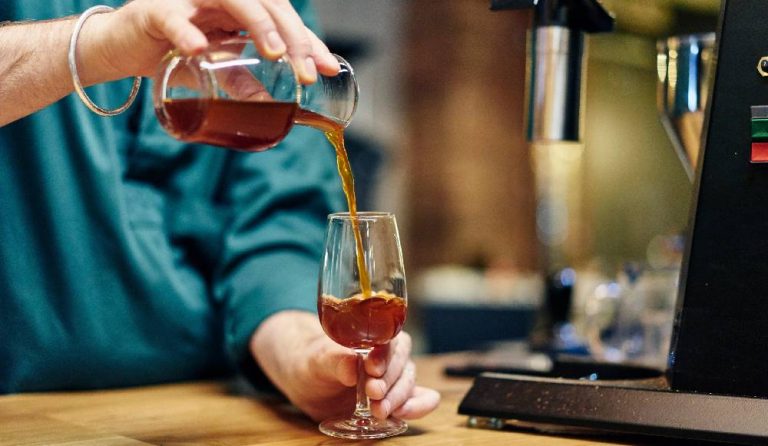 A barista pouring a glass cold brew coffee