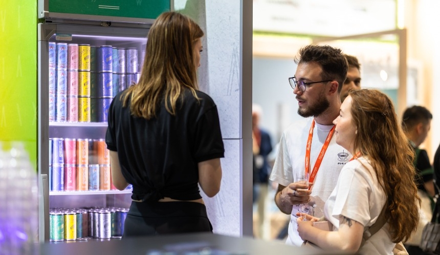 Three people talking in front of a fridge containing RTD drinks.