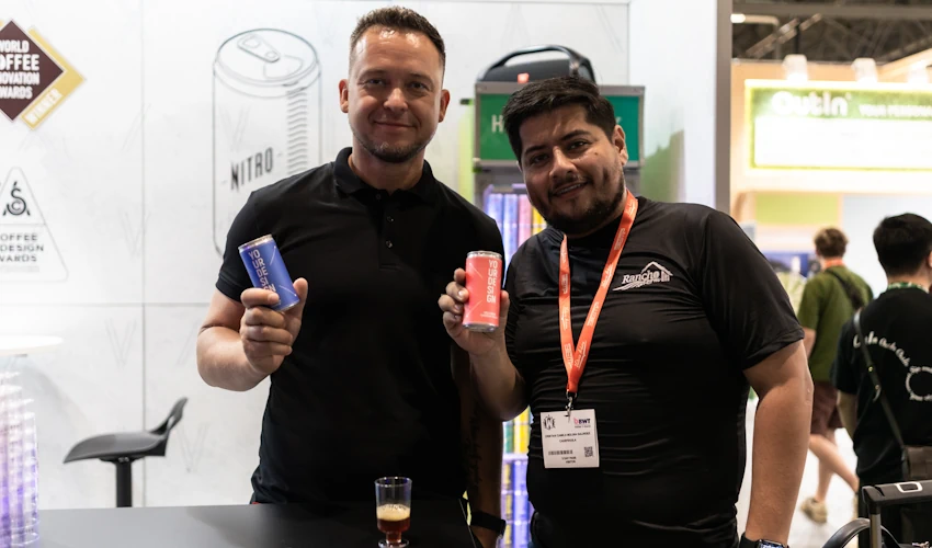 Two people holding canned cold brew at Hardtank's World of Coffee Copenhagen trade show booth.