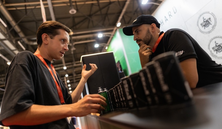 Two people stood speaking in front of a collection of wholesale cold brew RTDs.